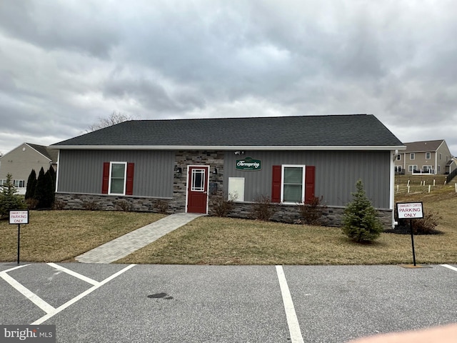 view of front of home featuring stone siding, roof with shingles, uncovered parking, and a front yard