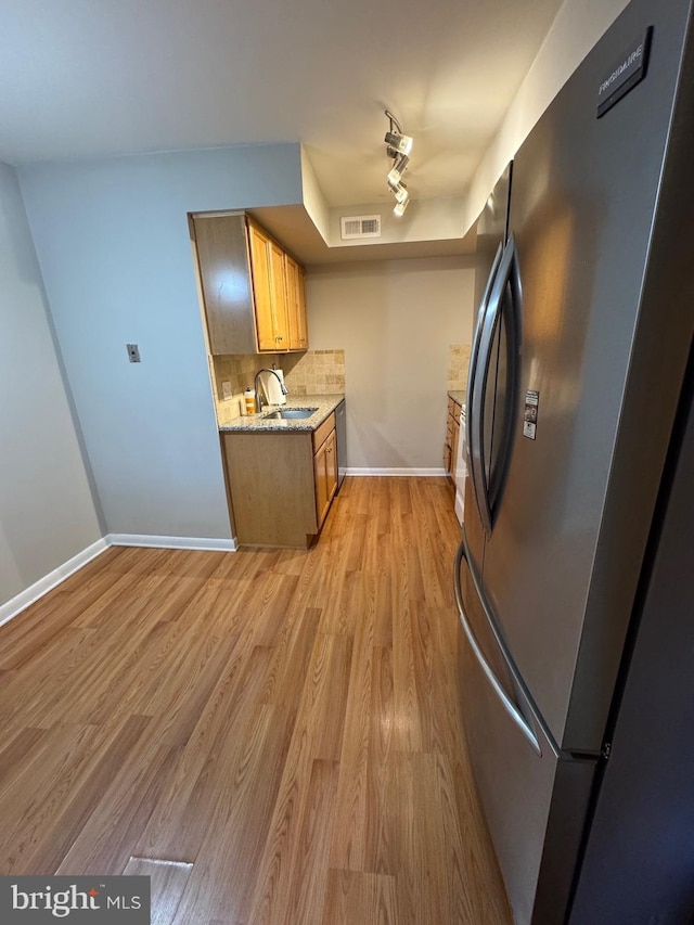 kitchen featuring decorative backsplash, appliances with stainless steel finishes, light stone counters, sink, and light hardwood / wood-style floors