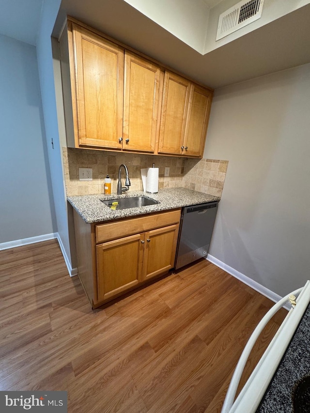 kitchen featuring stainless steel dishwasher, light hardwood / wood-style floors, light stone counters, and sink