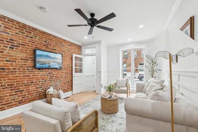 living room with light hardwood / wood-style floors, brick wall, crown molding, and ceiling fan