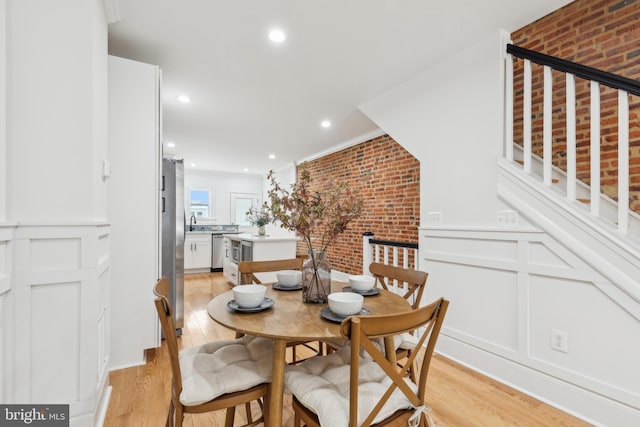 dining space with light wood-type flooring and brick wall