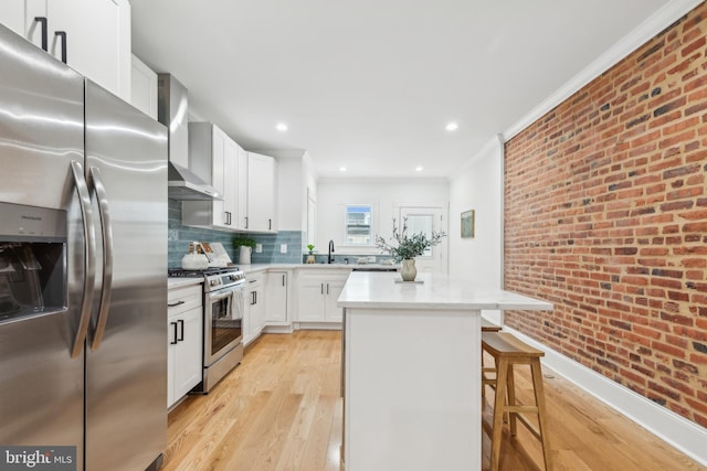 kitchen featuring brick wall, appliances with stainless steel finishes, a center island, white cabinetry, and a breakfast bar