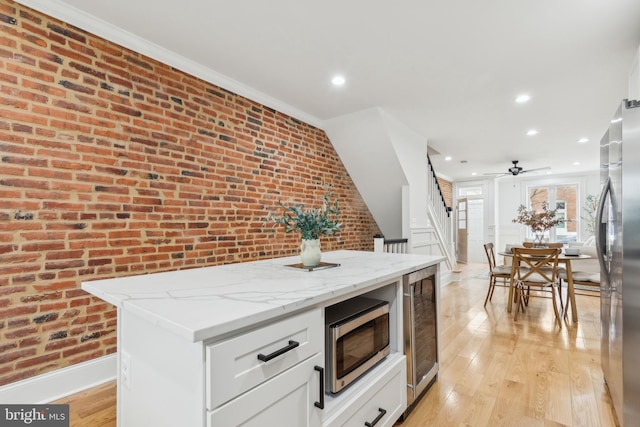 kitchen with a kitchen island, stainless steel appliances, white cabinets, brick wall, and light stone counters