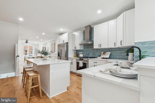 kitchen with white cabinetry, stainless steel appliances, a center island, wall chimney range hood, and sink