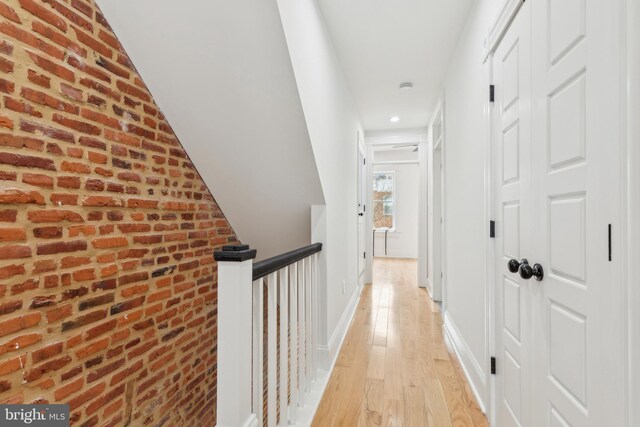 hall featuring brick wall and light hardwood / wood-style flooring