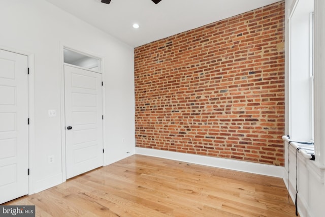 unfurnished bedroom featuring hardwood / wood-style flooring, brick wall, and ceiling fan