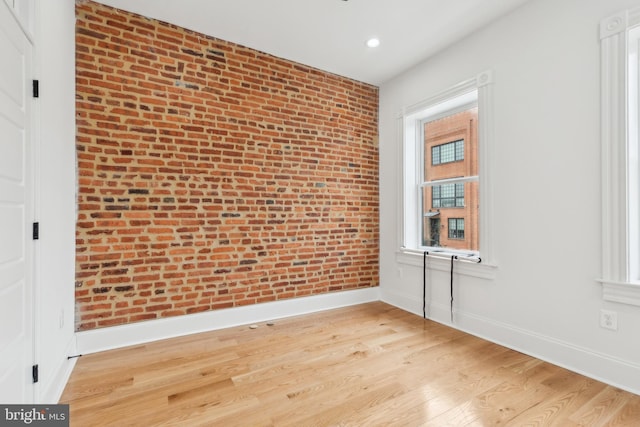 spare room featuring brick wall and light hardwood / wood-style floors