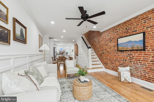 living room featuring wood-type flooring, brick wall, crown molding, and ceiling fan