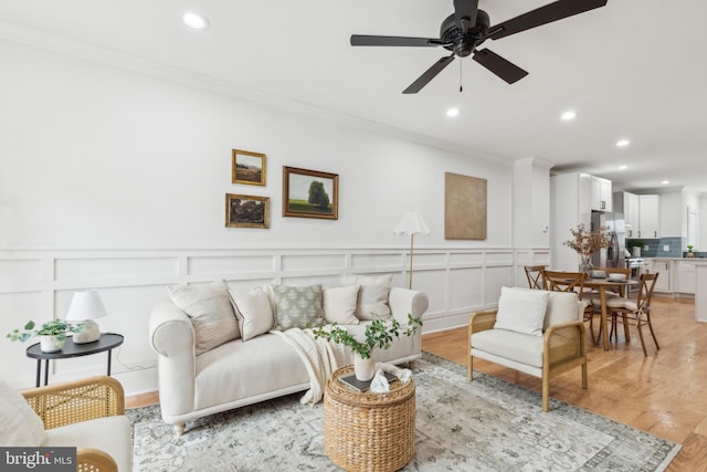 living room with ceiling fan, light wood-type flooring, and ornamental molding