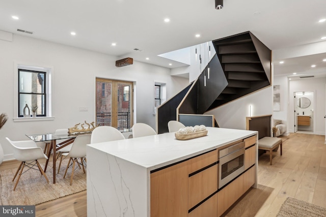 kitchen featuring stainless steel microwave, light stone counters, light hardwood / wood-style floors, and a large island