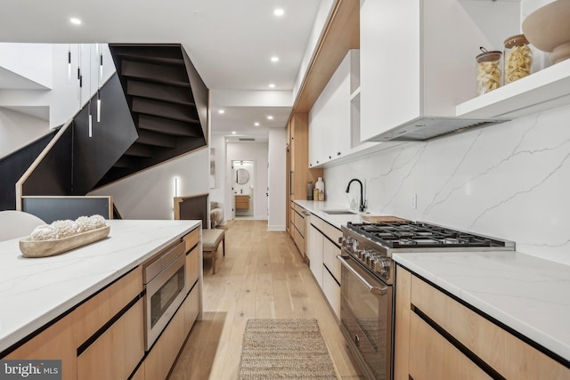 kitchen with white cabinetry, stainless steel appliances, light hardwood / wood-style flooring, light stone counters, and sink