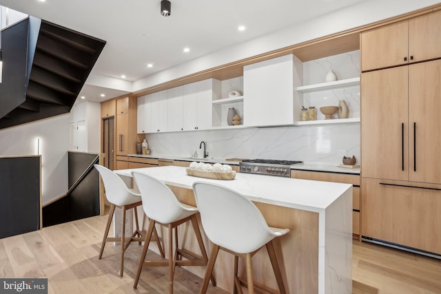 kitchen with range, a kitchen island, backsplash, light hardwood / wood-style flooring, and a breakfast bar area