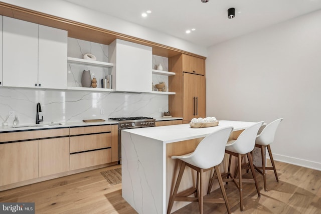 kitchen featuring white cabinetry, tasteful backsplash, light wood-type flooring, gas range, and sink