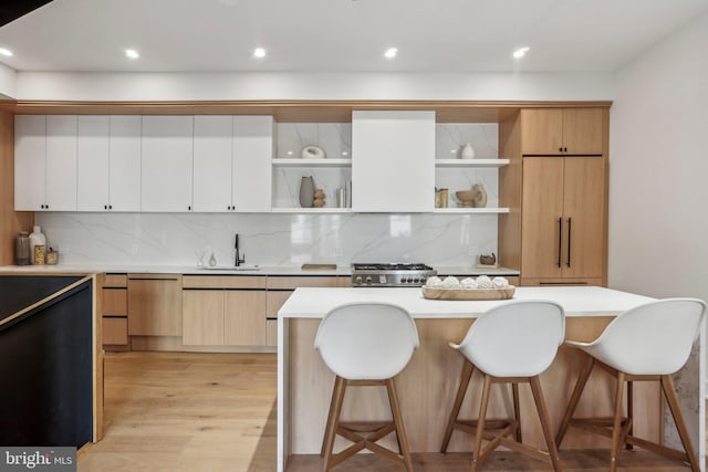 kitchen featuring white cabinetry, tasteful backsplash, sink, light wood-type flooring, and a center island