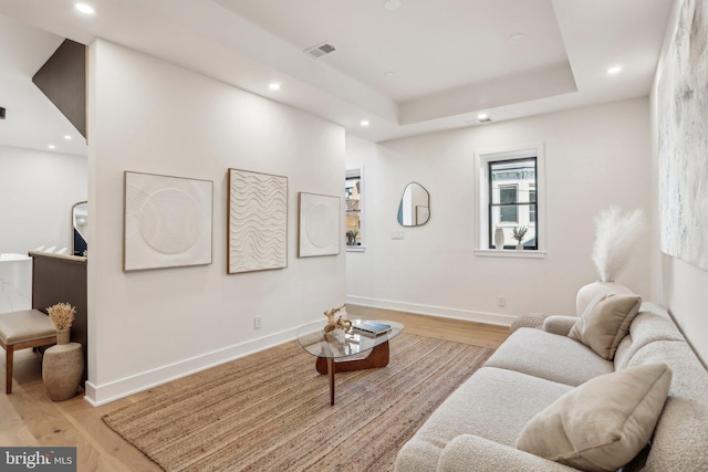 living room with a raised ceiling and light wood-type flooring