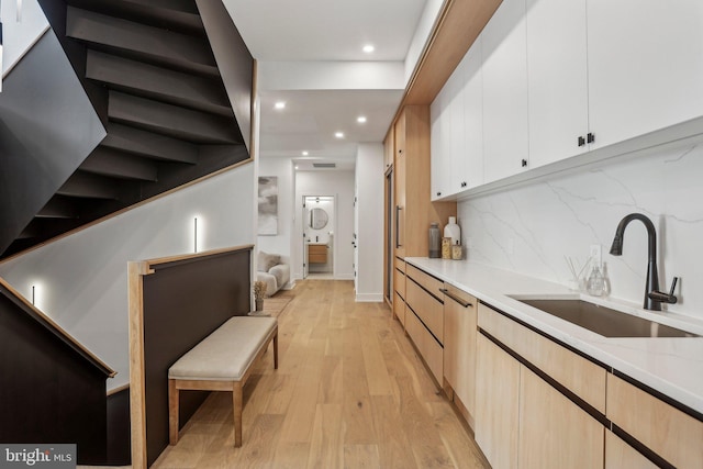 kitchen with backsplash, sink, white cabinetry, light hardwood / wood-style flooring, and light stone counters