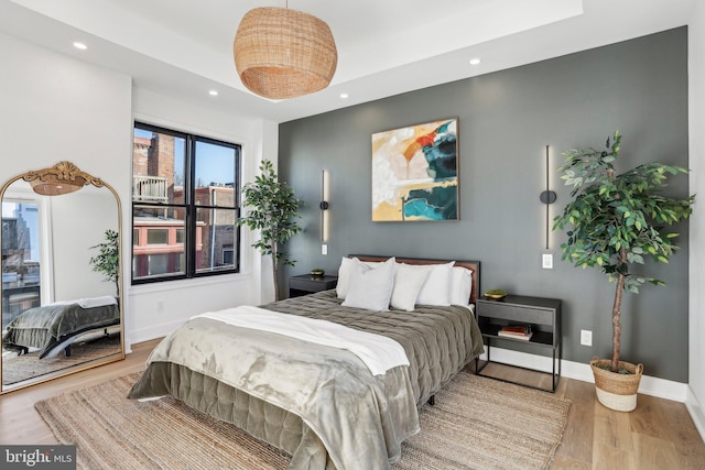 bedroom with light wood-type flooring and a tray ceiling