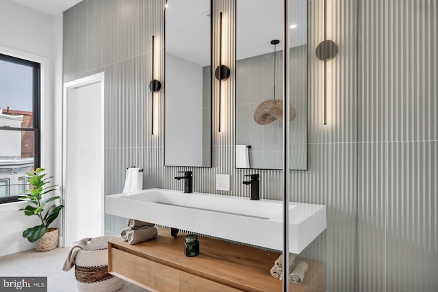 bathroom with a shower with shower door, sink, and tile walls