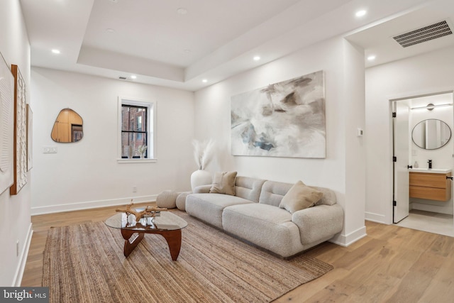 living room featuring a raised ceiling, light wood-type flooring, and sink