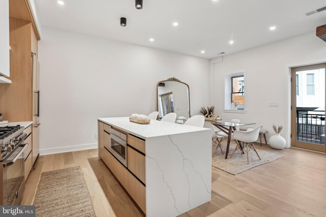 kitchen featuring a kitchen island, light wood-type flooring, stainless steel appliances, light brown cabinetry, and light stone counters