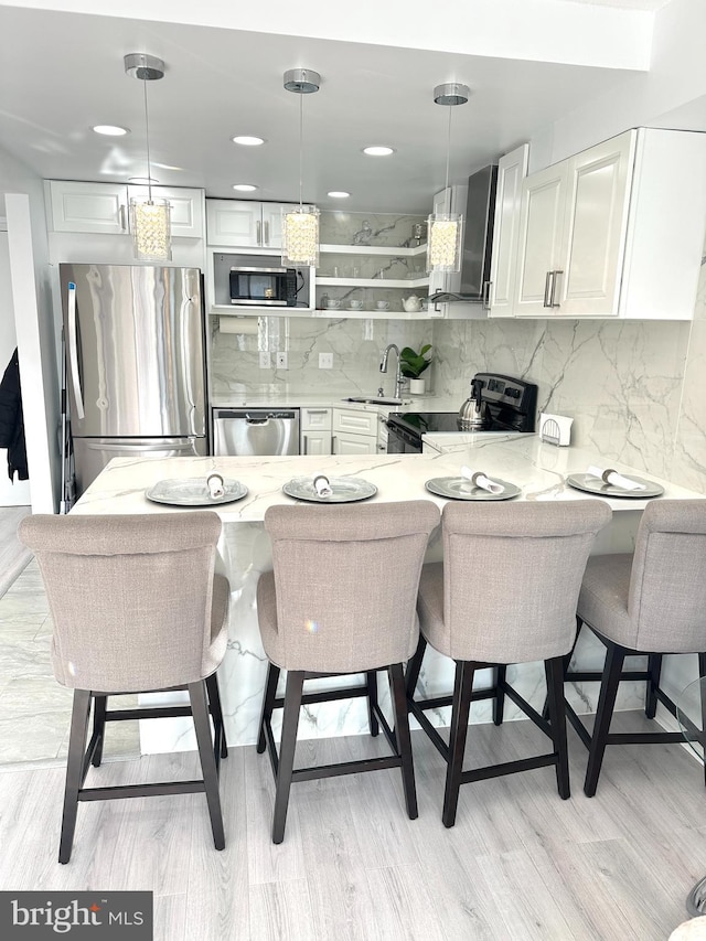 kitchen featuring pendant lighting, kitchen peninsula, wall chimney range hood, a breakfast bar, and appliances with stainless steel finishes