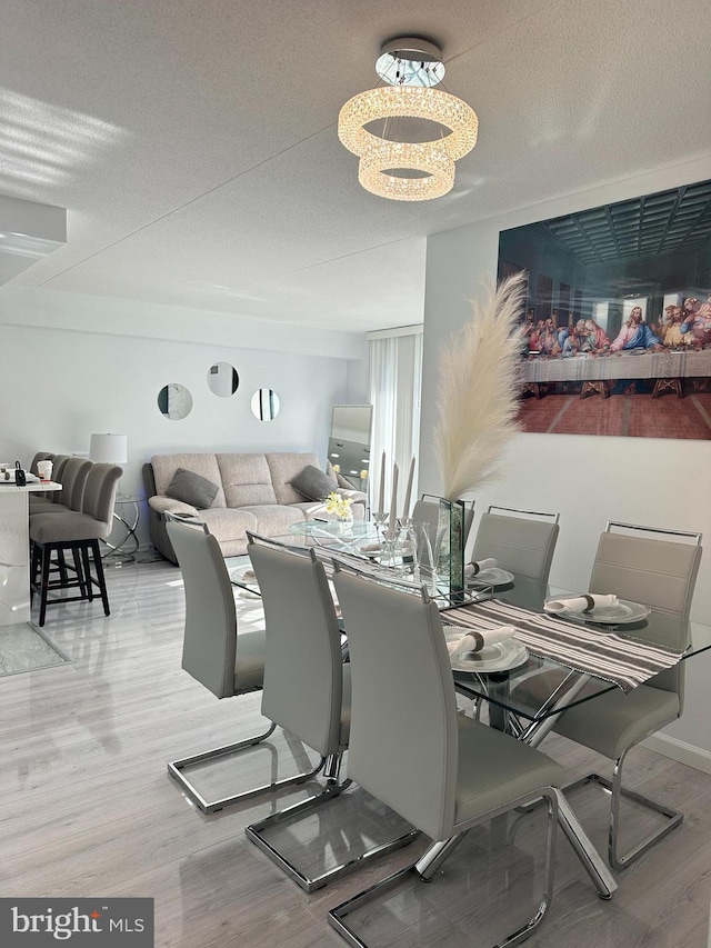 dining area with wood-type flooring, an inviting chandelier, and a textured ceiling