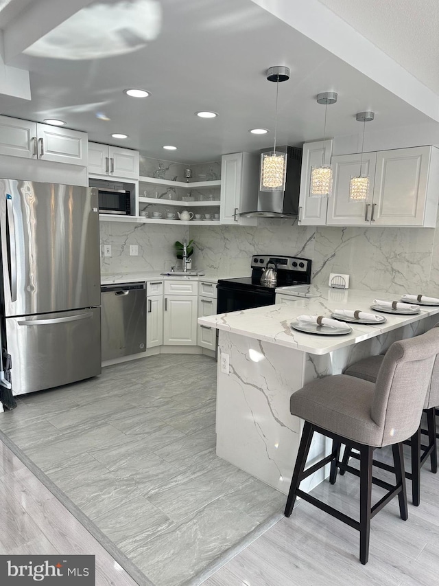 kitchen featuring decorative light fixtures, white cabinetry, wall chimney exhaust hood, kitchen peninsula, and appliances with stainless steel finishes