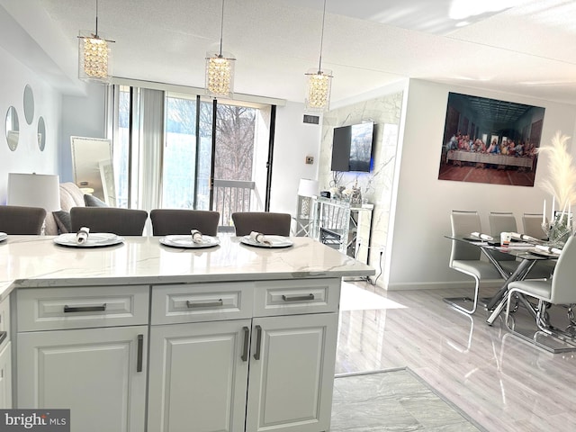 kitchen featuring light stone countertops, light hardwood / wood-style flooring, and hanging light fixtures