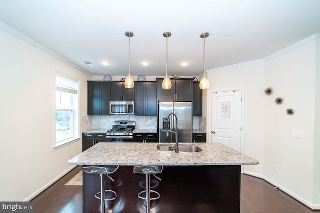 kitchen with light stone counters, decorative light fixtures, stainless steel appliances, and a center island with sink