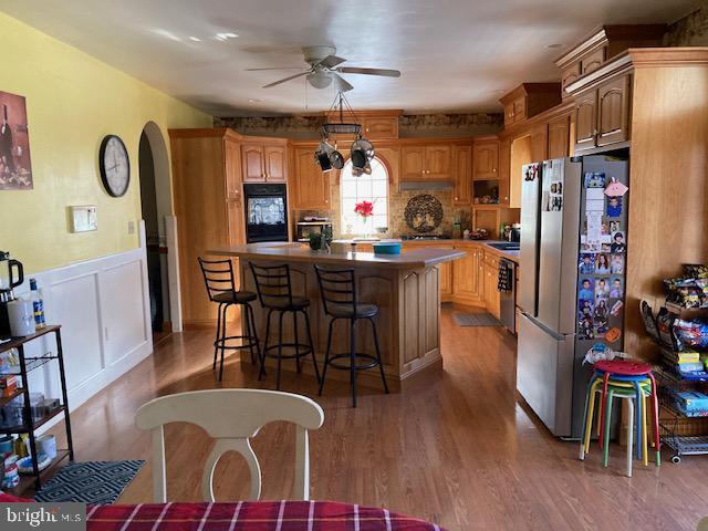 kitchen with hardwood / wood-style floors, a kitchen breakfast bar, ceiling fan, stainless steel fridge, and a kitchen island