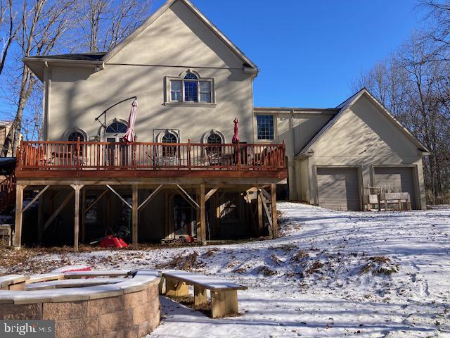 snow covered back of property featuring a garage and a deck