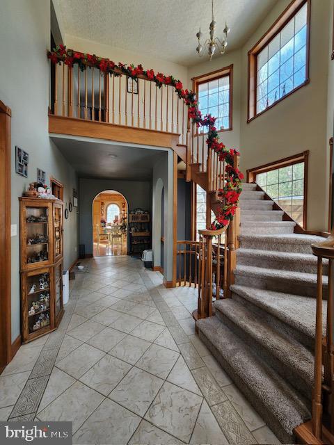 foyer with a high ceiling, a textured ceiling, an inviting chandelier, and a healthy amount of sunlight