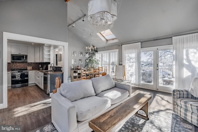 living room with vaulted ceiling with skylight, track lighting, sink, dark hardwood / wood-style floors, and a chandelier