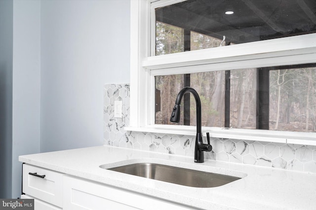 details featuring light stone counters, white cabinetry, tasteful backsplash, and sink