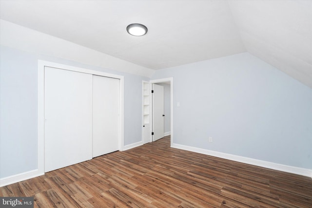 unfurnished bedroom with lofted ceiling, a closet, and dark wood-type flooring