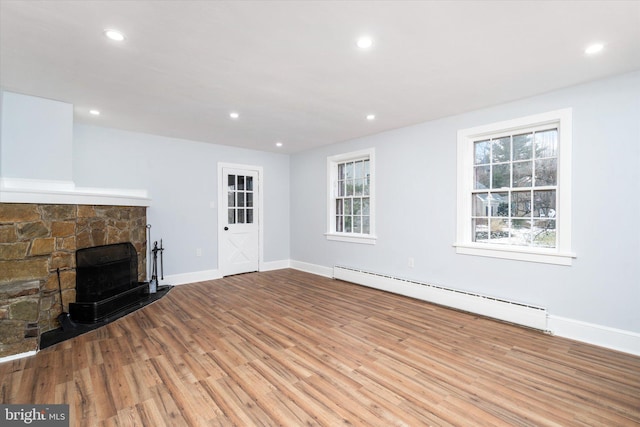 unfurnished living room with a stone fireplace, light hardwood / wood-style flooring, and a baseboard heating unit