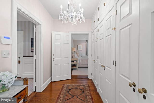 hall with dark wood-type flooring and a chandelier