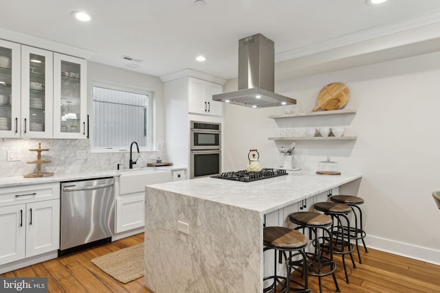 kitchen with a breakfast bar, island exhaust hood, stainless steel appliances, white cabinetry, and a sink