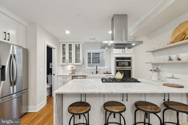 kitchen featuring island range hood, a sink, white cabinets, appliances with stainless steel finishes, and backsplash