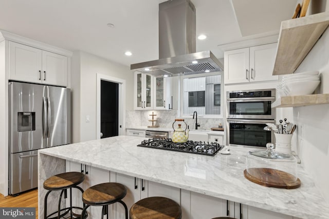 kitchen featuring stainless steel appliances, a breakfast bar, white cabinetry, and island exhaust hood