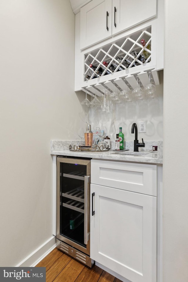 bar featuring beverage cooler, baseboards, wood finished floors, wet bar, and a sink