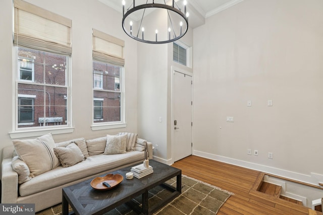 living area featuring wood finished floors, visible vents, baseboards, ornamental molding, and an inviting chandelier