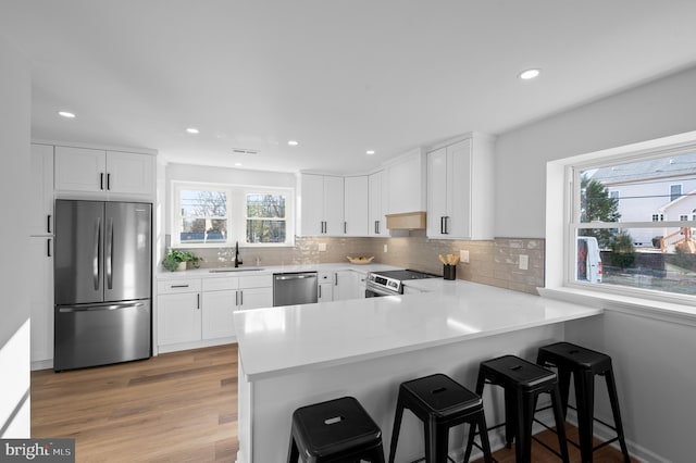 kitchen featuring a kitchen breakfast bar, kitchen peninsula, white cabinets, and appliances with stainless steel finishes