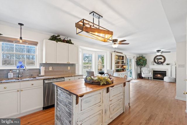 kitchen with sink, wooden counters, decorative light fixtures, stainless steel dishwasher, and white cabinets