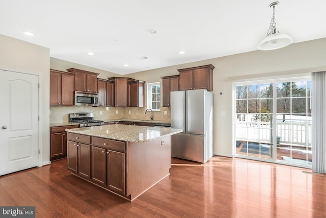 kitchen with pendant lighting, dark hardwood / wood-style flooring, a center island, stainless steel appliances, and light stone countertops