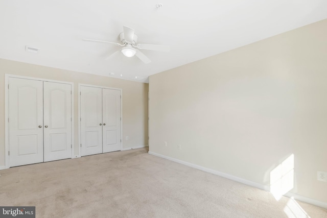 unfurnished bedroom featuring multiple closets, light carpet, and ceiling fan