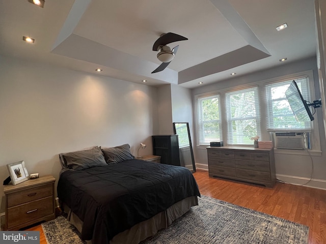 bedroom featuring cooling unit, ceiling fan, light hardwood / wood-style floors, and a raised ceiling