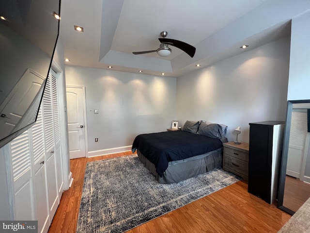 bedroom with ceiling fan, a closet, hardwood / wood-style floors, and a tray ceiling