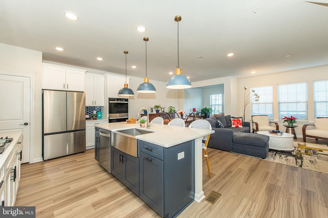 kitchen featuring sink, white cabinets, light hardwood / wood-style flooring, hanging light fixtures, and appliances with stainless steel finishes