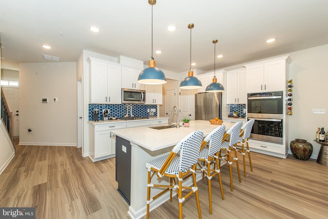 kitchen featuring stainless steel appliances, white cabinetry, sink, and hanging light fixtures